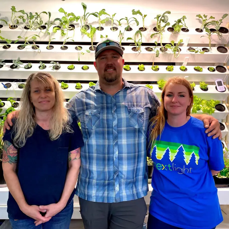 Three people standing in front of a wall filled with plants.